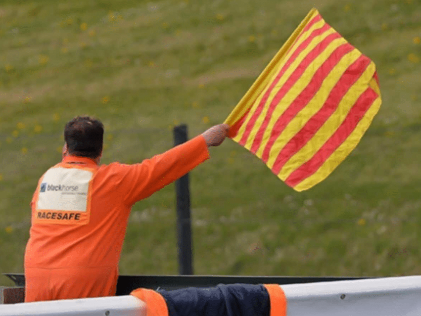 Marshal waving a yellow flag with red stripes