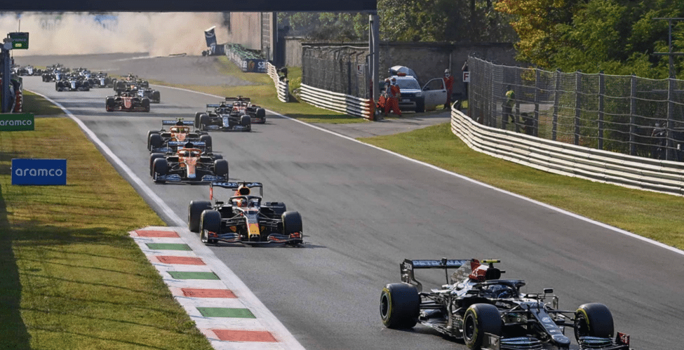 F1 cars racing through a corner at Monza with smoke in the background