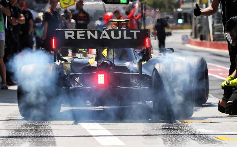 Renault F1 car leaving pit lane with smoking fresh tyres
